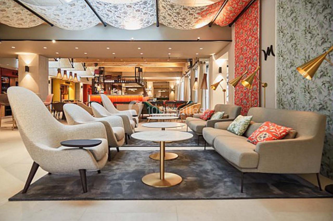 Espace salon moderne avec canapés beige, tables basses rondes et éclairage design dans un intérieur lumineux.