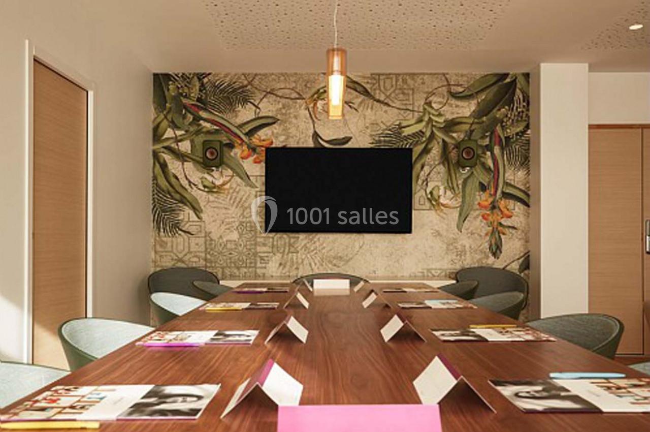 Salle de réunion avec une grande table en bois, des chaises modernes, un écran mural et une décoration tropicale.
