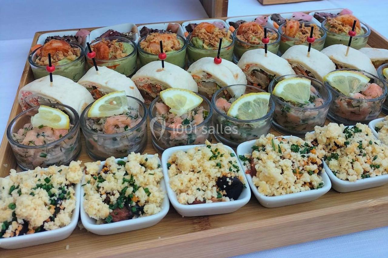 Plateau de verrines, mini-sandwichs et plats individuels variés, disposés sur une table pour un buffet.