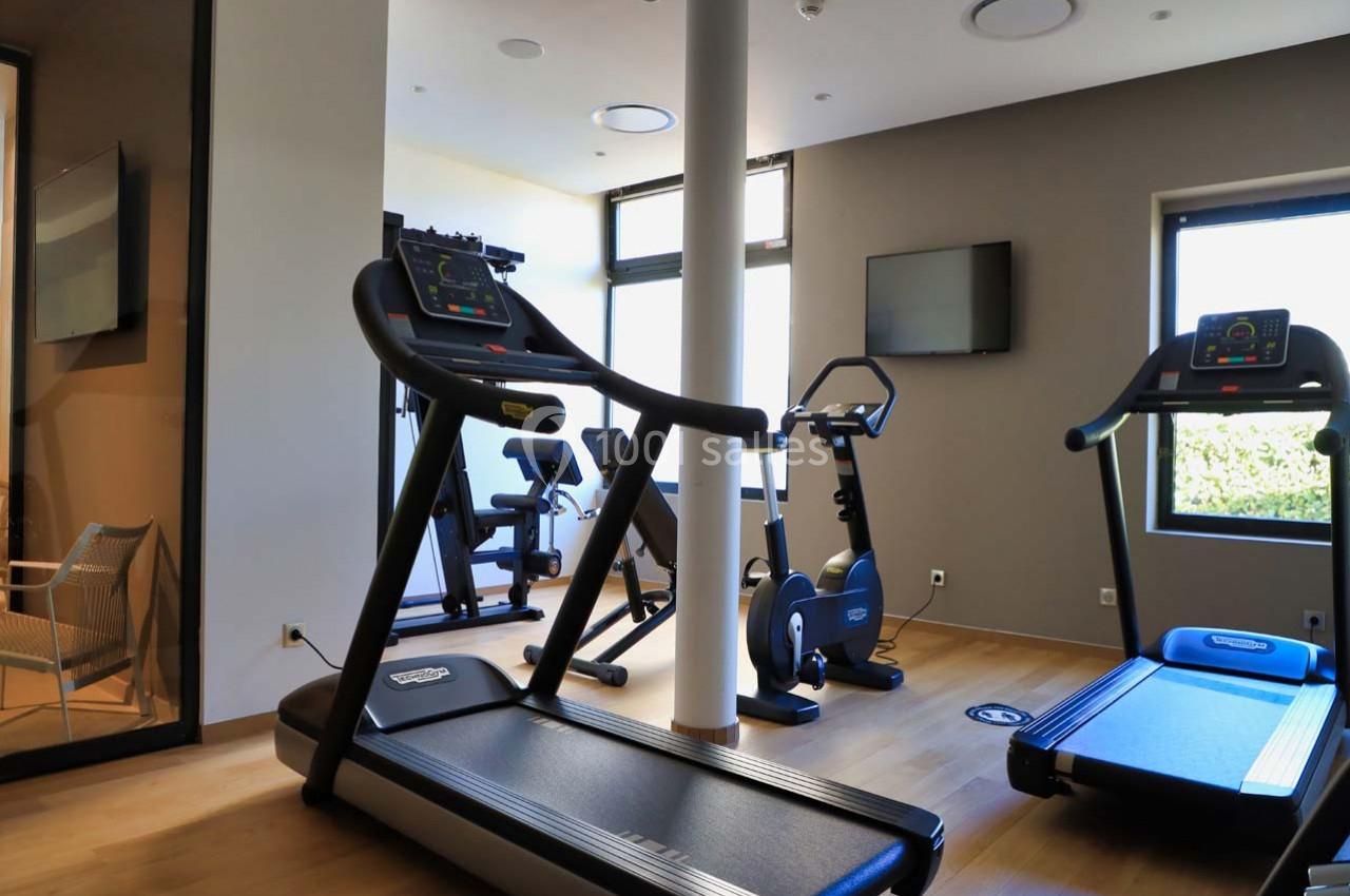Salle de sport lumineuse avec tapis de course, vélos d'exercice et équipements de fitness modernes.