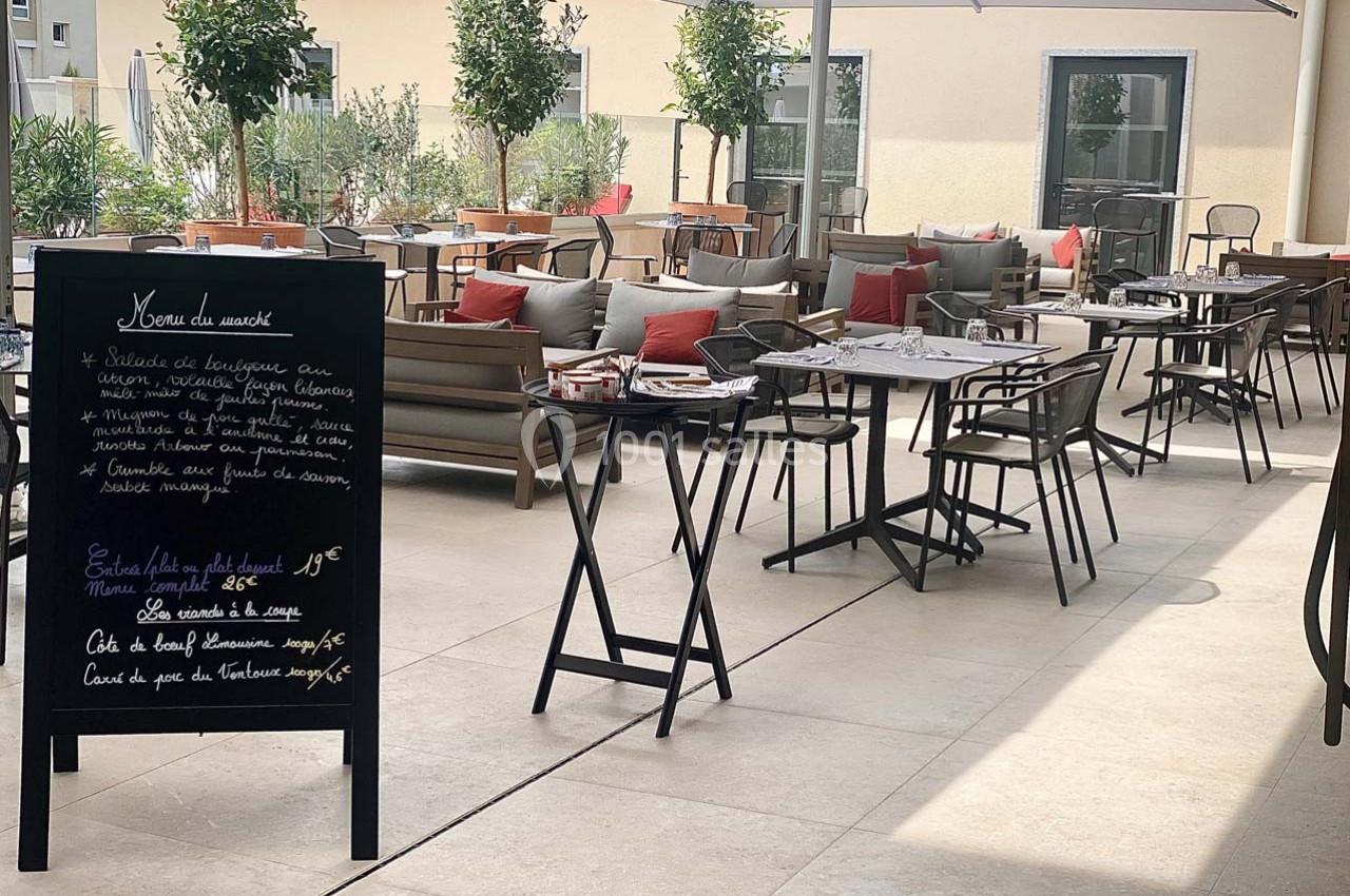 Terrasse d'un restaurant avec des tables dressées, un tableau noir affichant le menu et des parasols pour l'ombre.