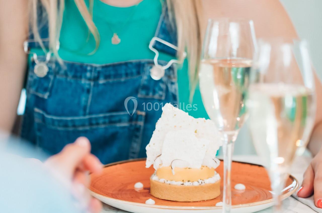 Une personne devant une tartelette garnie de meringue, entourée de verres de champagne sur une table.