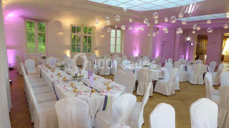 Salle de réception décorée avec des tables dressées, nappes blanches et éclairage rose tamisé.