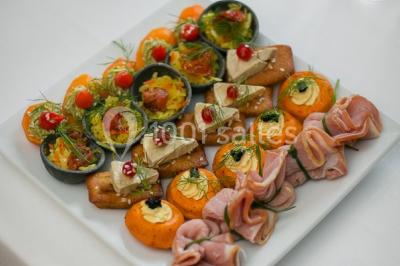 Plateau de canapés variés avec charcuterie, fromage, légumes et garnitures, présenté sur une table blanche.
