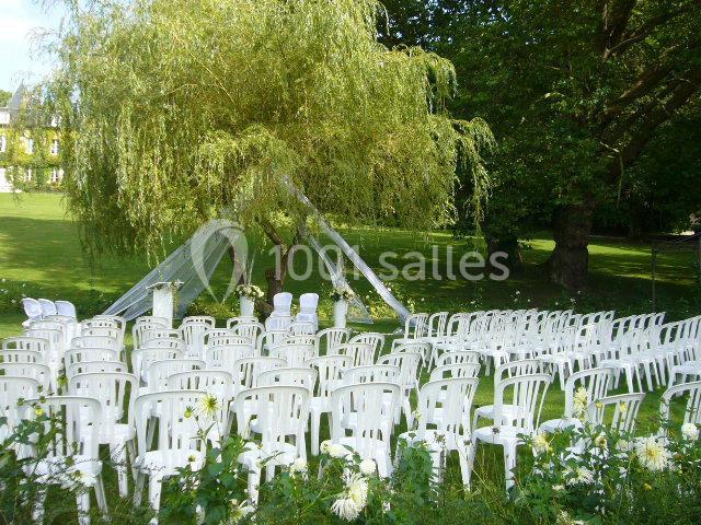 Chaises blanches disposées en rangées devant une arche décorée, installées dans un jardin verdoyant pour une cérémonie.