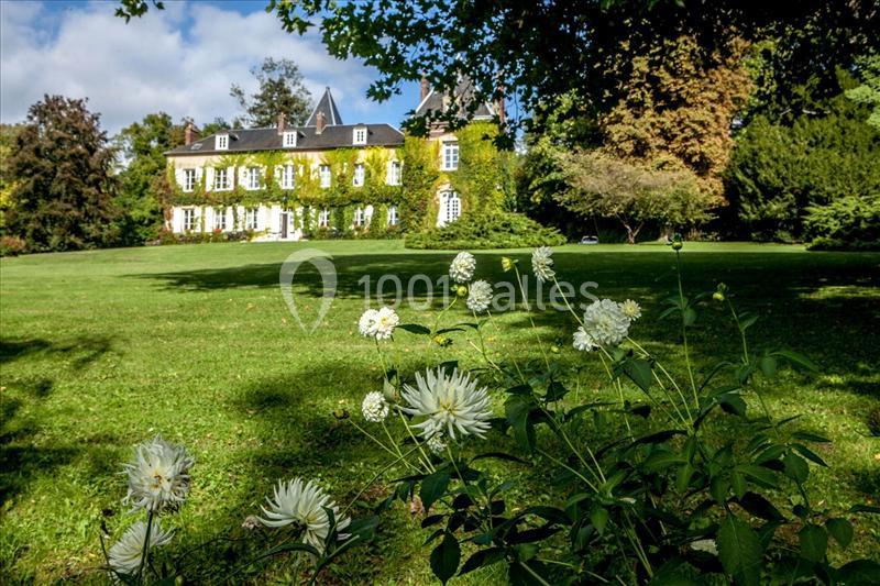 Manoir entouré de verdure avec une pelouse et des fleurs blanches au premier plan, sous un ciel partiellement nuageux.
