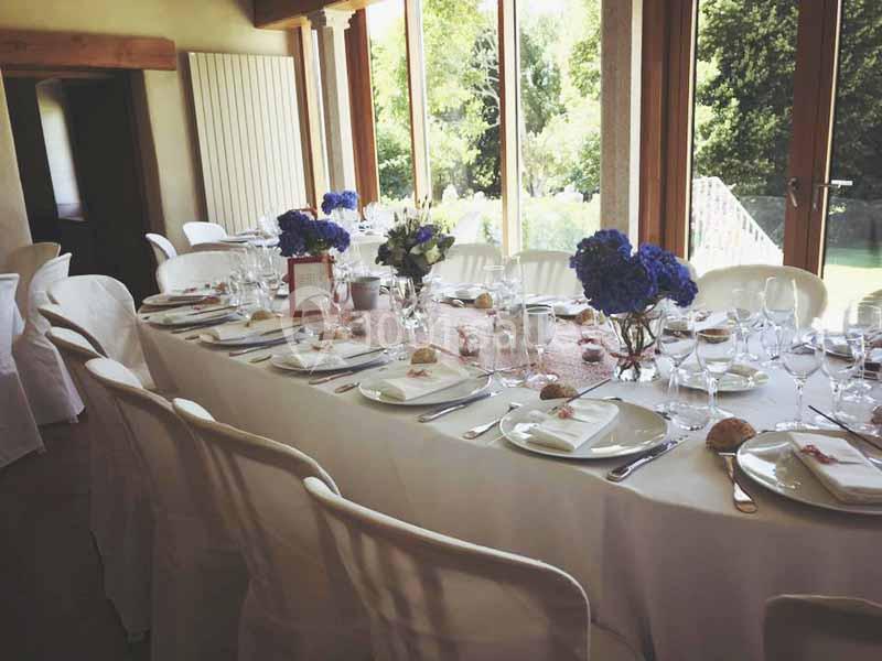 Location salle Audierne (Finistère) - Manoir de Menez Bras #5 Table dressée pour un repas, avec nappes blanches, vaisselle élégante et bouquets de fleurs bleues, près de grandes fenêtres.