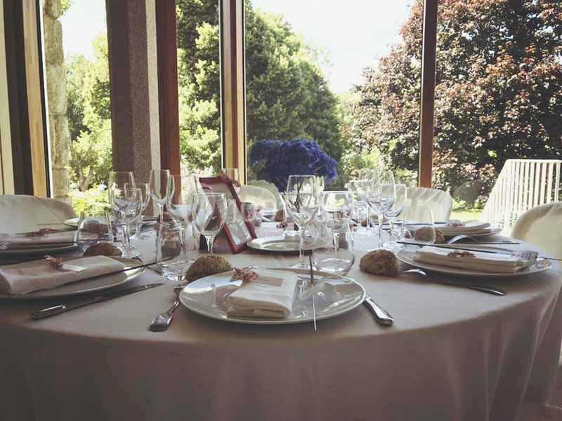 Location salle Audierne (Finistère) - Manoir de Menez Bras #6 Table élégamment dressée avec nappes blanches, vaisselle raffinée et vue sur un jardin arboré à travers de grandes baies…