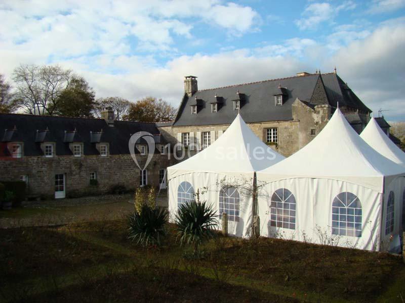 Location salle Audierne (Finistère) - Manoir de Menez Bras #3 Tentes blanches installées dans la cour d'un bâtiment en pierre de style traditionnel sous un ciel partiellement nuageux.