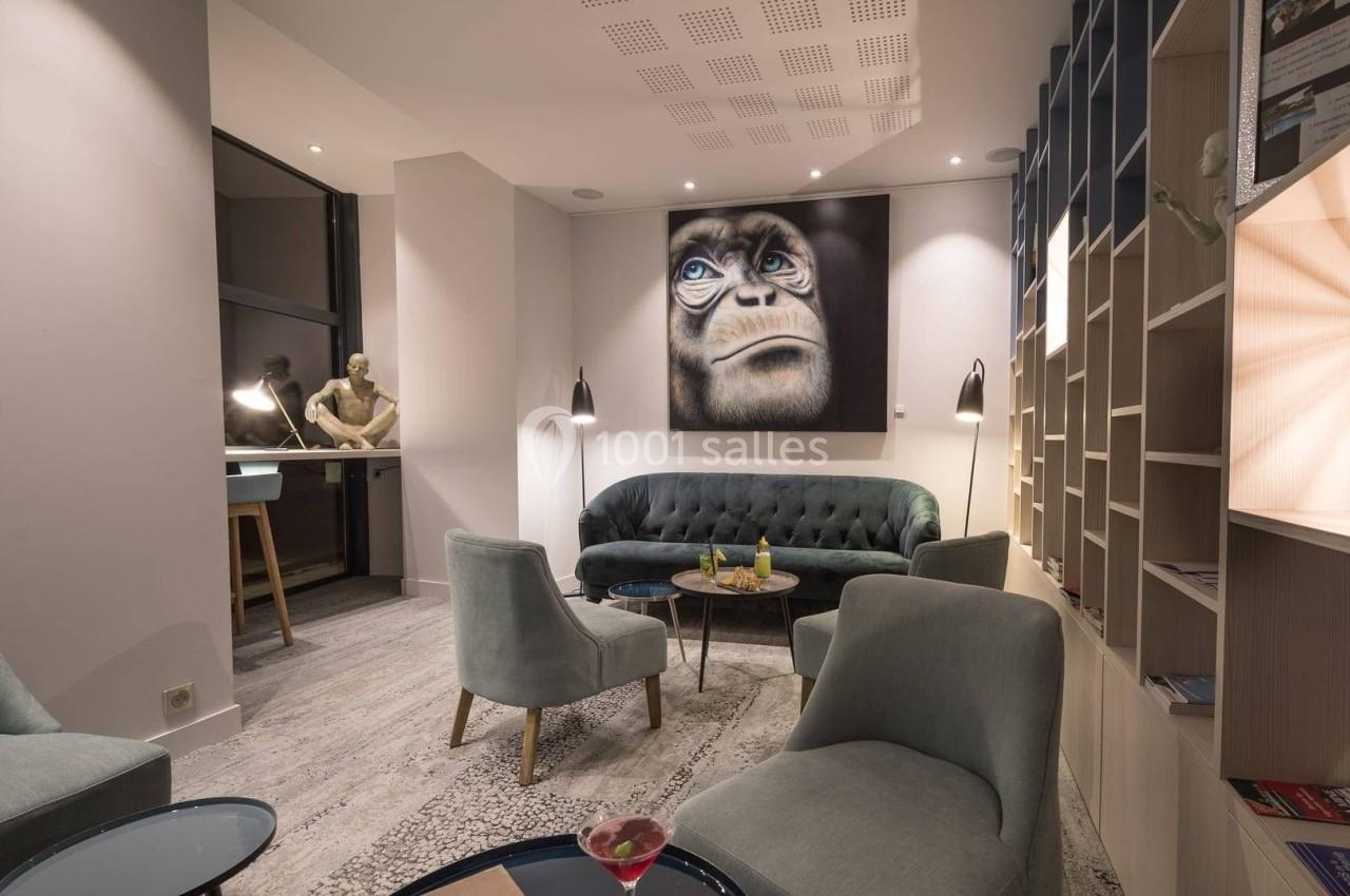 Salon moderne avec fauteuils, canapé, tables basses et décoration murale représentant un visage de singe.