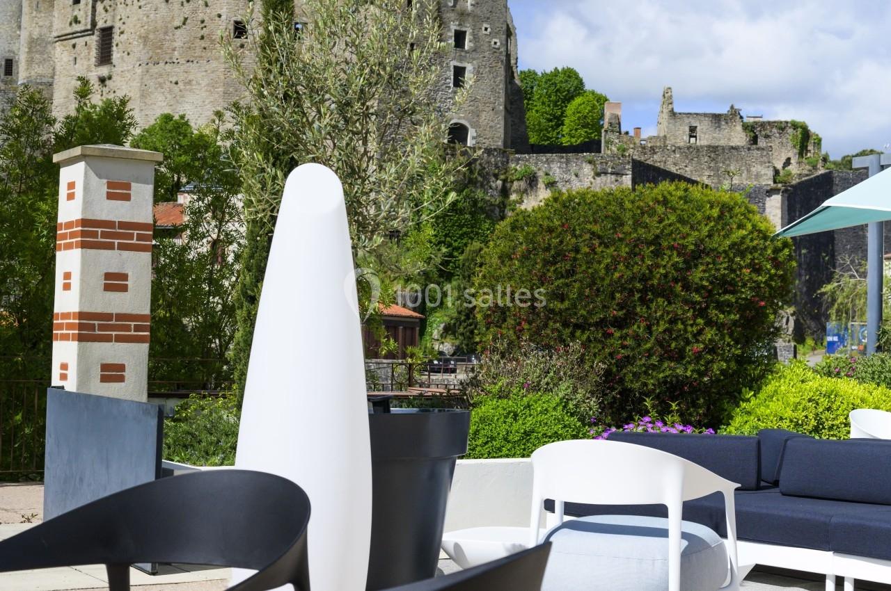 Mobilier de terrasse moderne avec vue sur un château médiéval sous un ciel bleu partiellement nuageux.