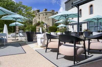 Mobilier de terrasse moderne avec vue sur un château médiéval sous un ciel bleu partiellement nuageux.