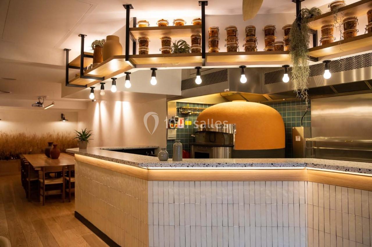Intérieur d'un restaurant avec un four à pizza en terre cuite, un comptoir carrelé et des étagères décorées de pots.