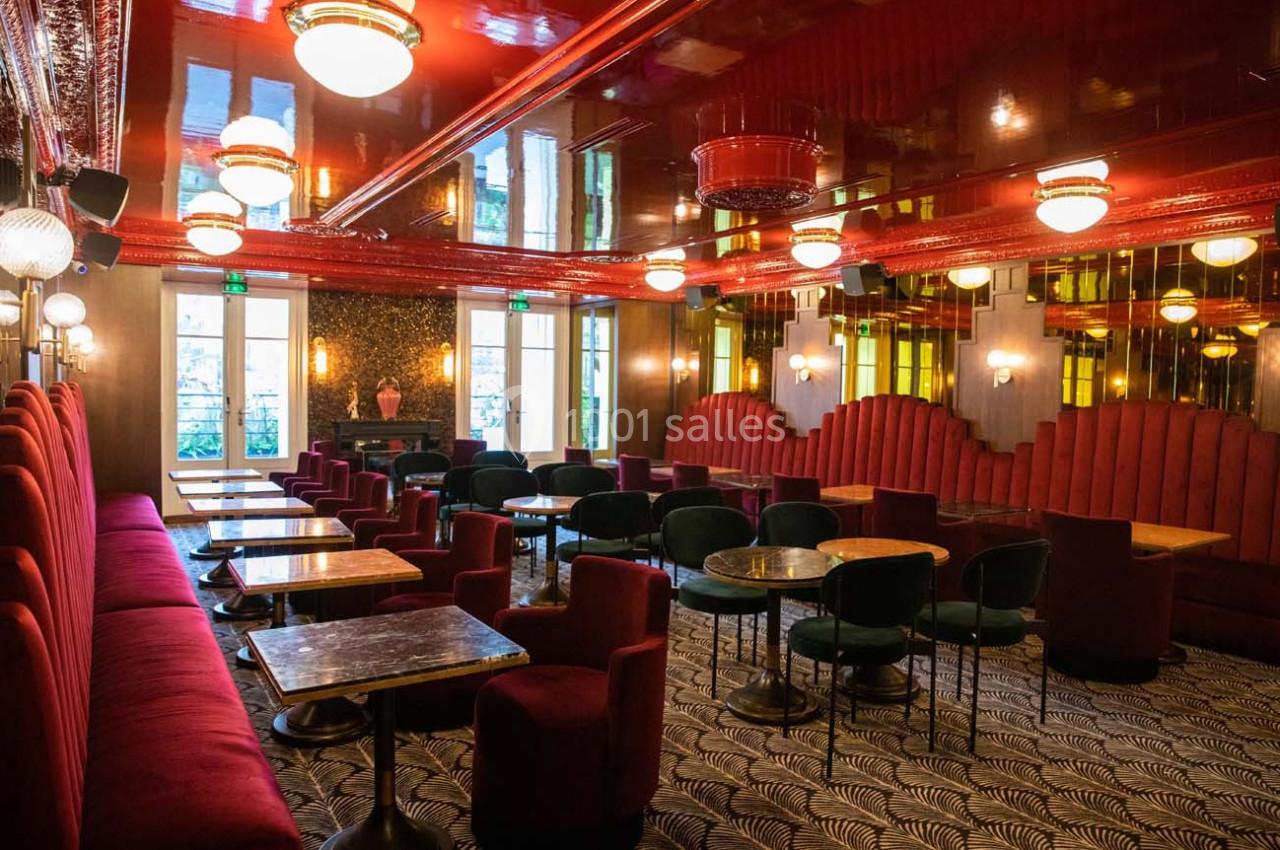 Salle élégante avec banquettes rouges, tables en marbre, chaises vertes et plafond brillant éclairé par des luminaires.