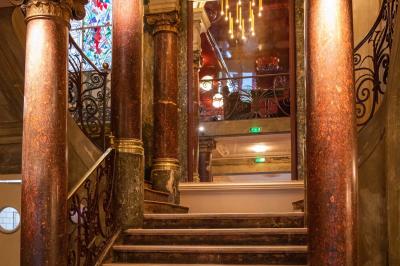 Escalier en marbre avec rampes en fer forgé, colonnes décoratives et lustres suspendus dans un intérieur ancien.