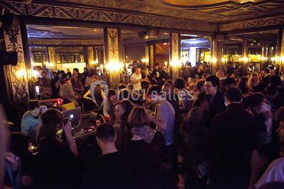 Groupe de personnes dans une salle ornée de miroirs et de lustres, avec un DJ jouant de la musique en arrière-plan.