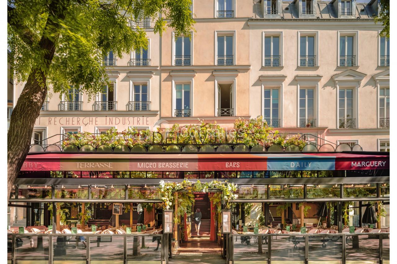 Façade d'une brasserie avec terrasse fleurie, située au rez-de-chaussée d'un immeuble haussmannien.