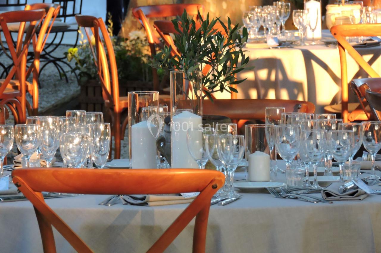 Table dressée en extérieur avec nappes blanches, verres, bougies et décoration végétale, éclairée par une lumière douce.