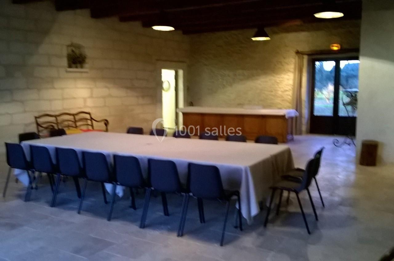 Salle avec une grande table rectangulaire recouverte d'une nappe blanche, entourée de chaises noires, éclairée par des…