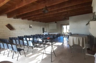Bâtisse ancienne en pierre avec volets rouges, entourée d'arbres, sous un ciel partiellement nuageux.