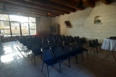 Bâtisse ancienne en pierre avec volets rouges, entourée d'arbres, sous un ciel partiellement nuageux.