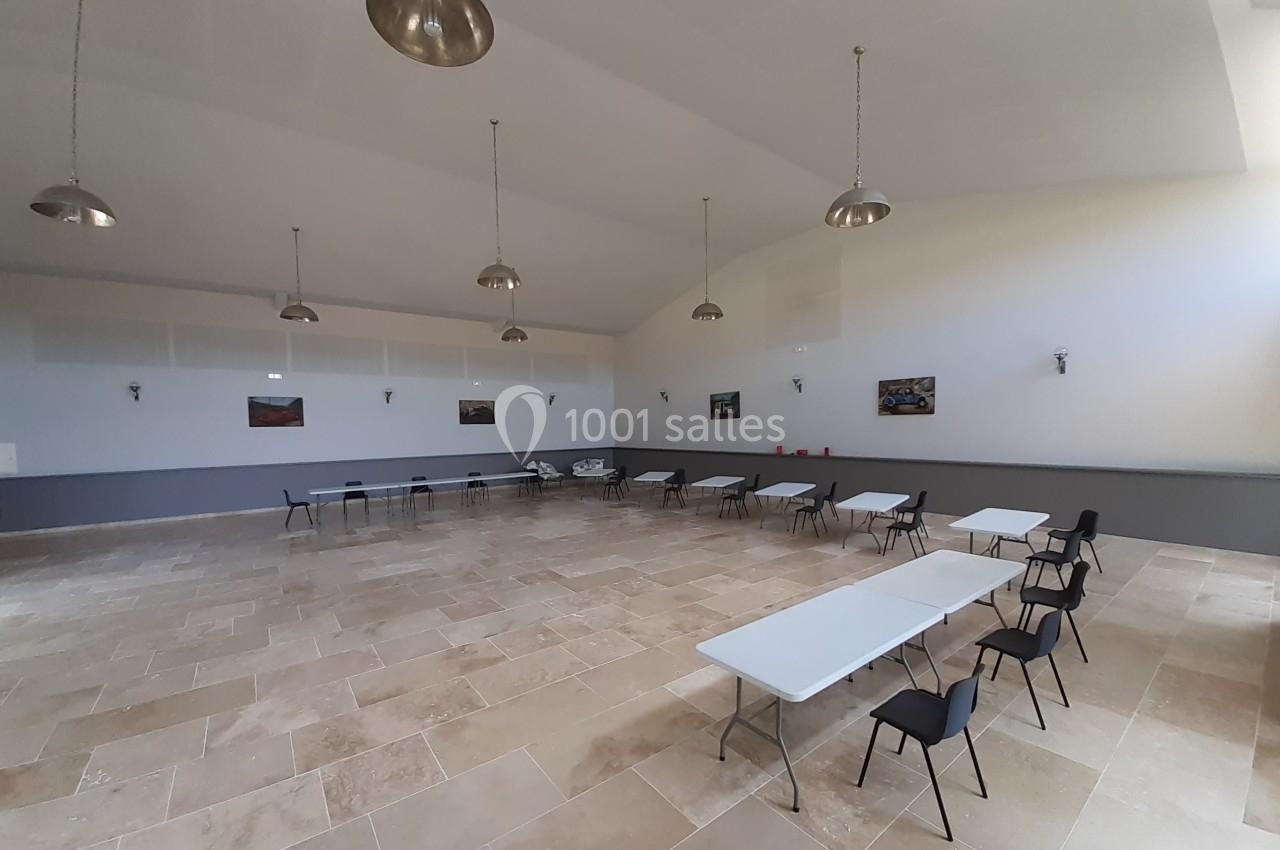 Salle spacieuse avec sol en carrelage clair, tables blanches et chaises noires, éclairée par des suspensions métalliques.