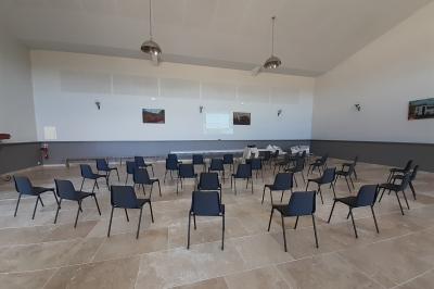 Bâtisse ancienne en pierre avec volets rouges, entourée d'arbres, sous un ciel partiellement nuageux.