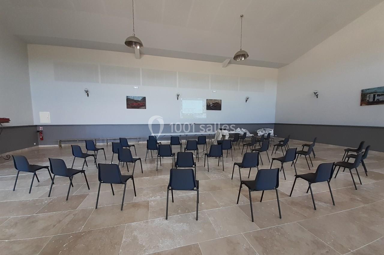 Salle vide avec des rangées de chaises noires disposées face à un écran de projection sur un mur clair.