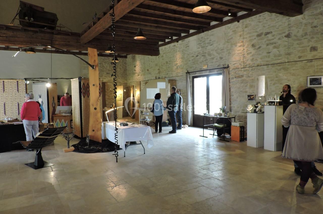 Salle d'exposition avec des œuvres d'art, des visiteurs et un éclairage naturel entrant par une grande porte vitrée.