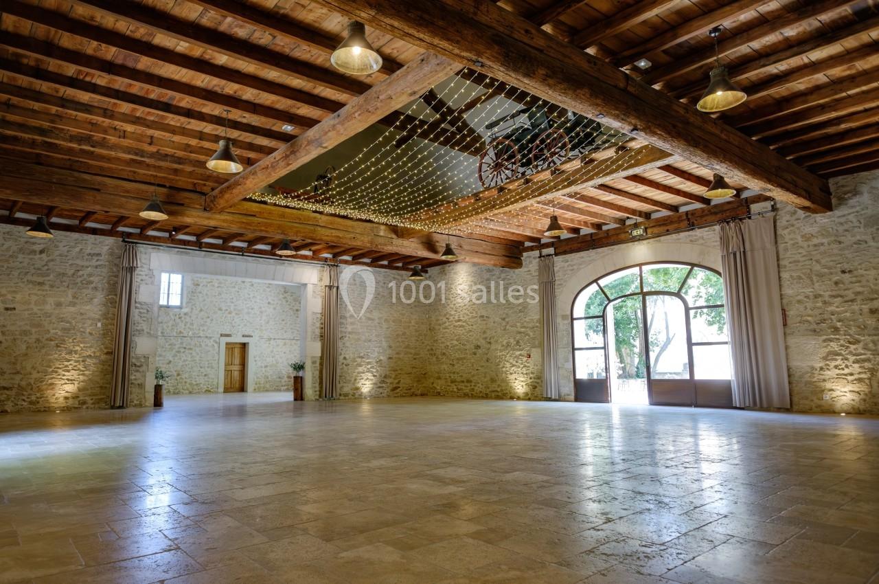 Salle spacieuse avec murs en pierre, plafond en bois, grandes fenêtres et guirlandes lumineuses suspendues.