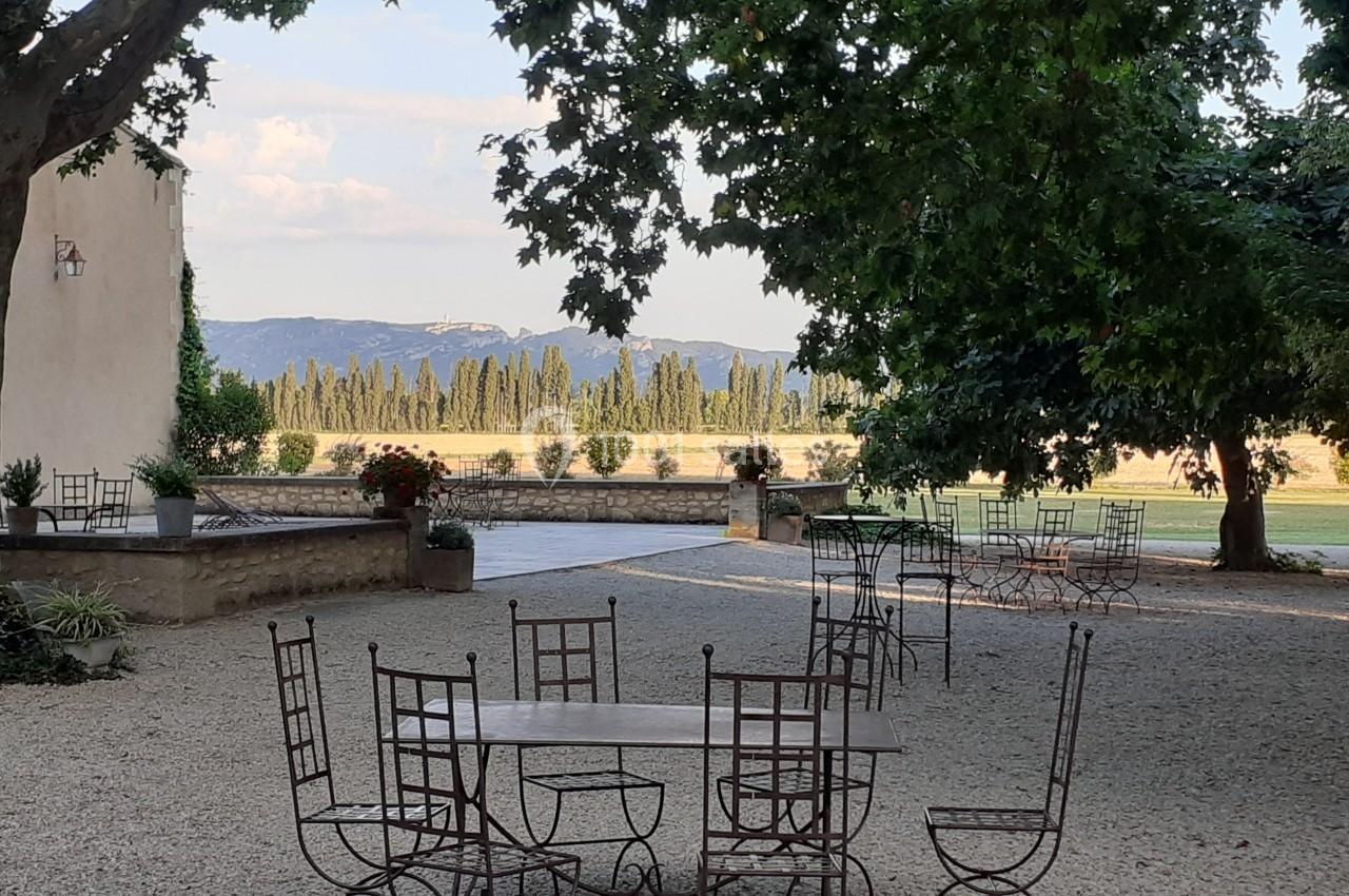 Tables et chaises en fer forgé disposées sur une terrasse ombragée avec vue sur des champs et des cyprès au loin.