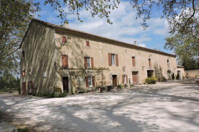 Bâtisse ancienne en pierre avec volets rouges, entourée d'arbres, sous un ciel partiellement nuageux.