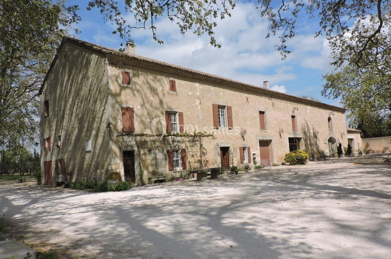 Bâtisse ancienne en pierre avec volets rouges, entourée d'arbres, sous un ciel partiellement nuageux.
