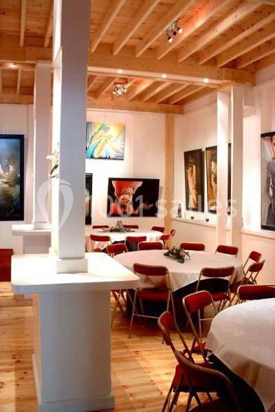 Salle lumineuse avec tables rondes dressées, chaises rouges et murs décorés de peintures modernes.