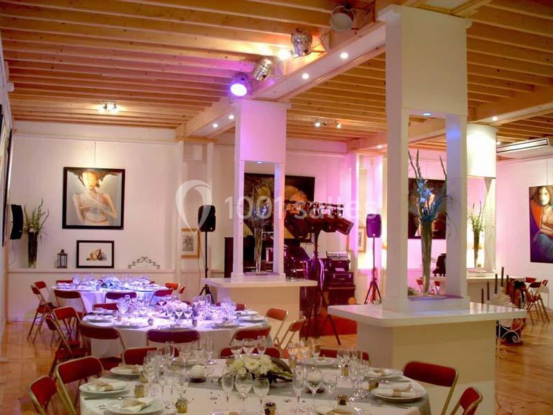 Salle de réception lumineuse avec tables dressées, chaises rouges et décorations murales artistiques.