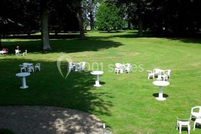 Terrasse en bois longeant un bâtiment en briques avec vue sur un jardin arboré sous un ciel bleu.