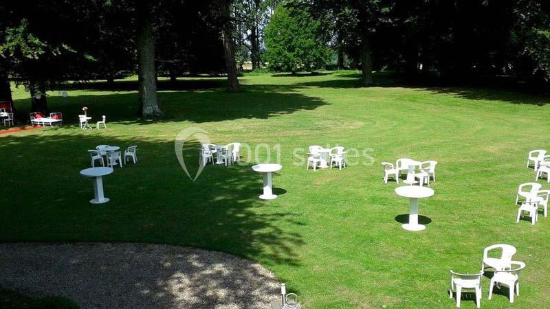 Chaises et tables blanches dispersées sur une pelouse verte entourée d'arbres, par une journée ensoleillée.