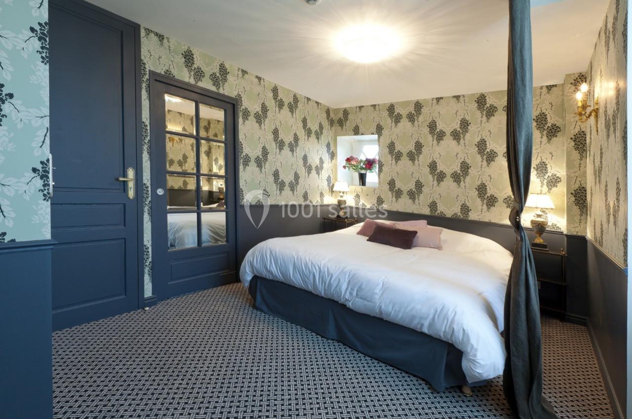 Chambre avec lit double, murs ornés de papier peint floral, miroir, éclairage doux et décoration classique.