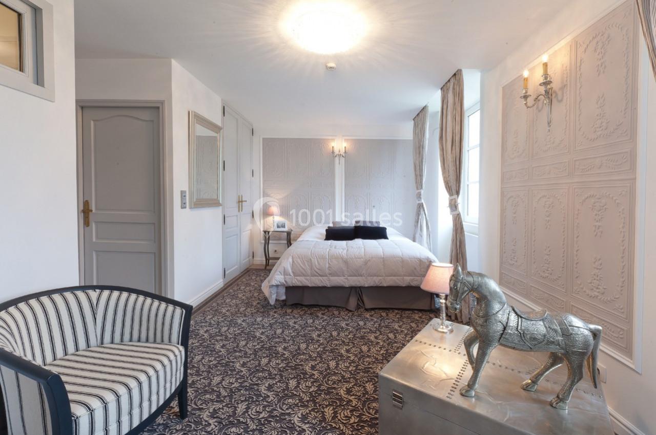 Chambre lumineuse avec lit double, fauteuil rayé, tapis à motifs et décoration élégante incluant un cheval argenté.