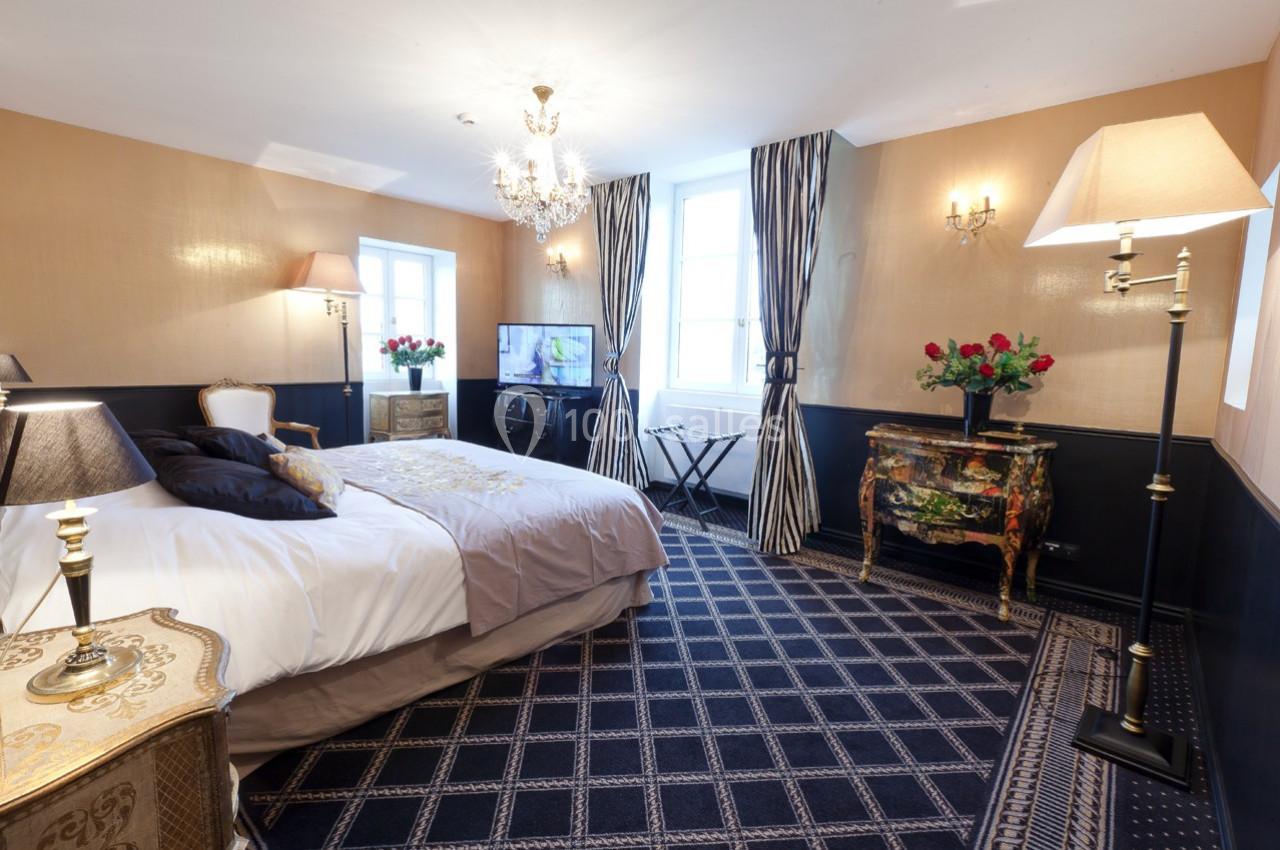 Chambre élégante avec lit double, mobilier classique, lustre, lampes, rideaux rayés et décorations florales.