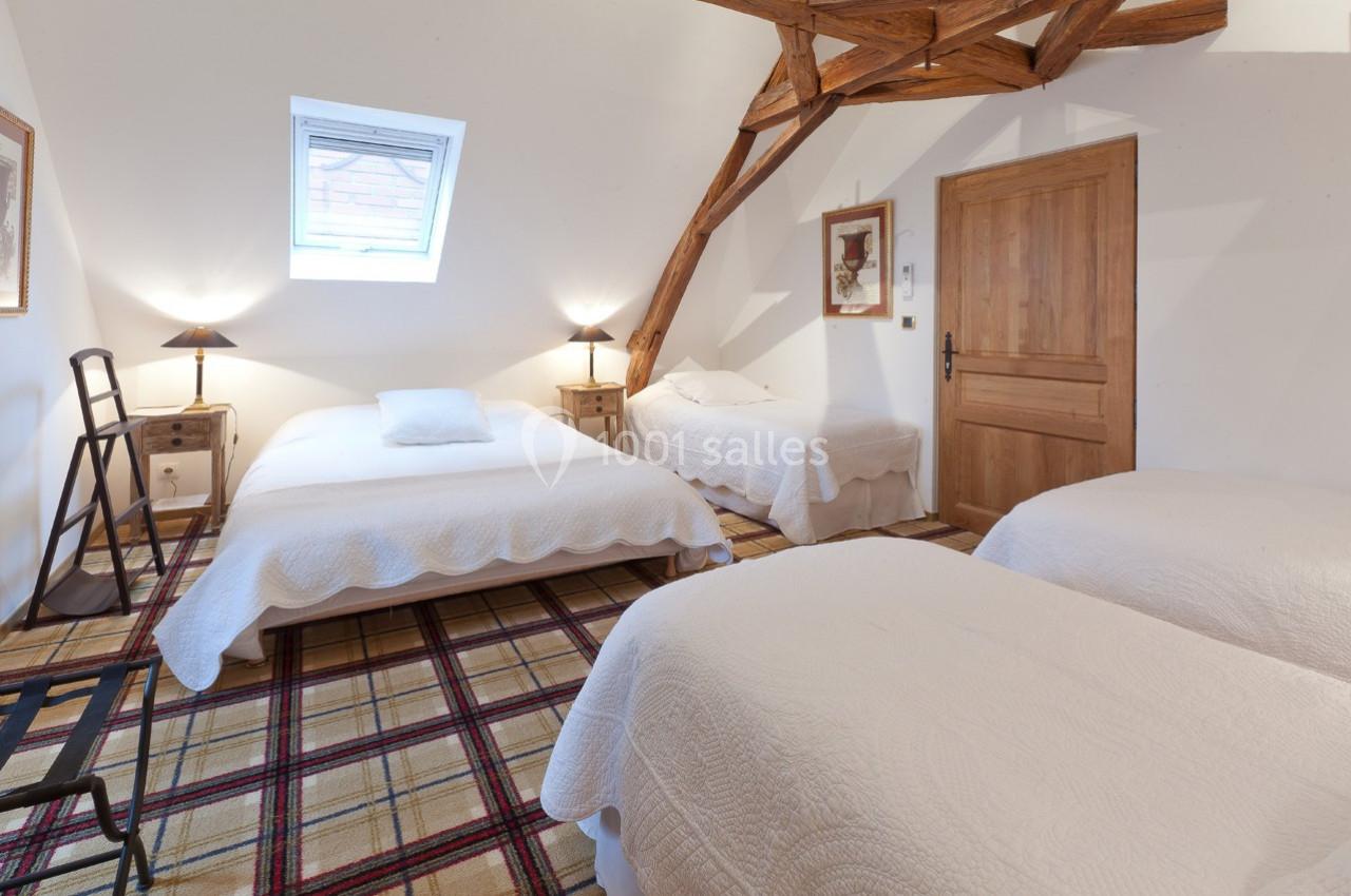 Chambre mansardée avec trois lits simples, décorée de poutres apparentes, éclairée par une fenêtre de toit.