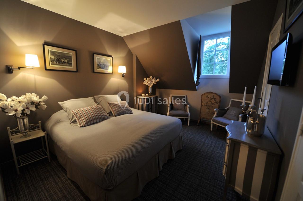 Chambre décorée avec des tons neutres, lit double, fauteuils, éclairage doux et fenêtre donnant sur des arbres.