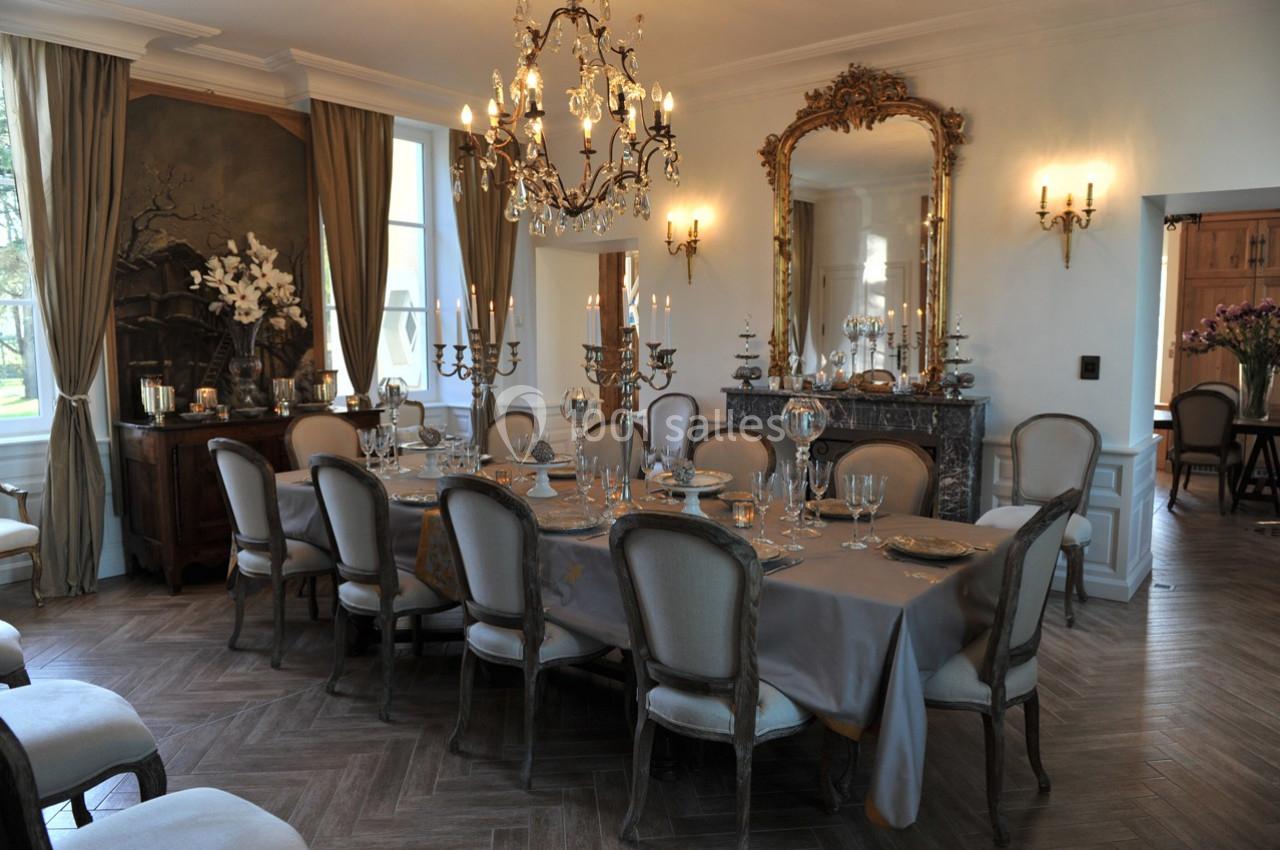 Salle à manger élégante avec une grande table dressée, des chandeliers, un miroir doré et des rideaux beiges.