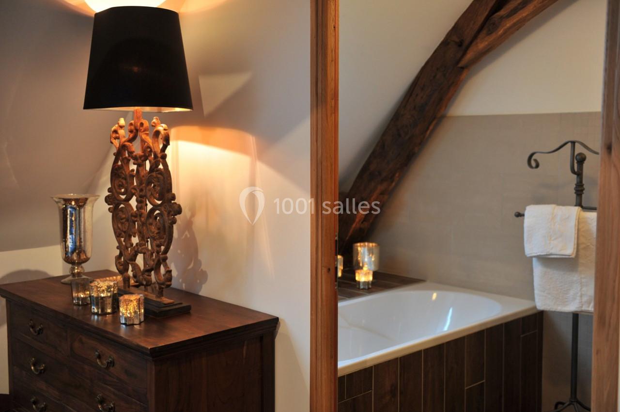 Salle de bain avec baignoire encastrée, poutres apparentes et meuble en bois surmonté d'une lampe décorative.