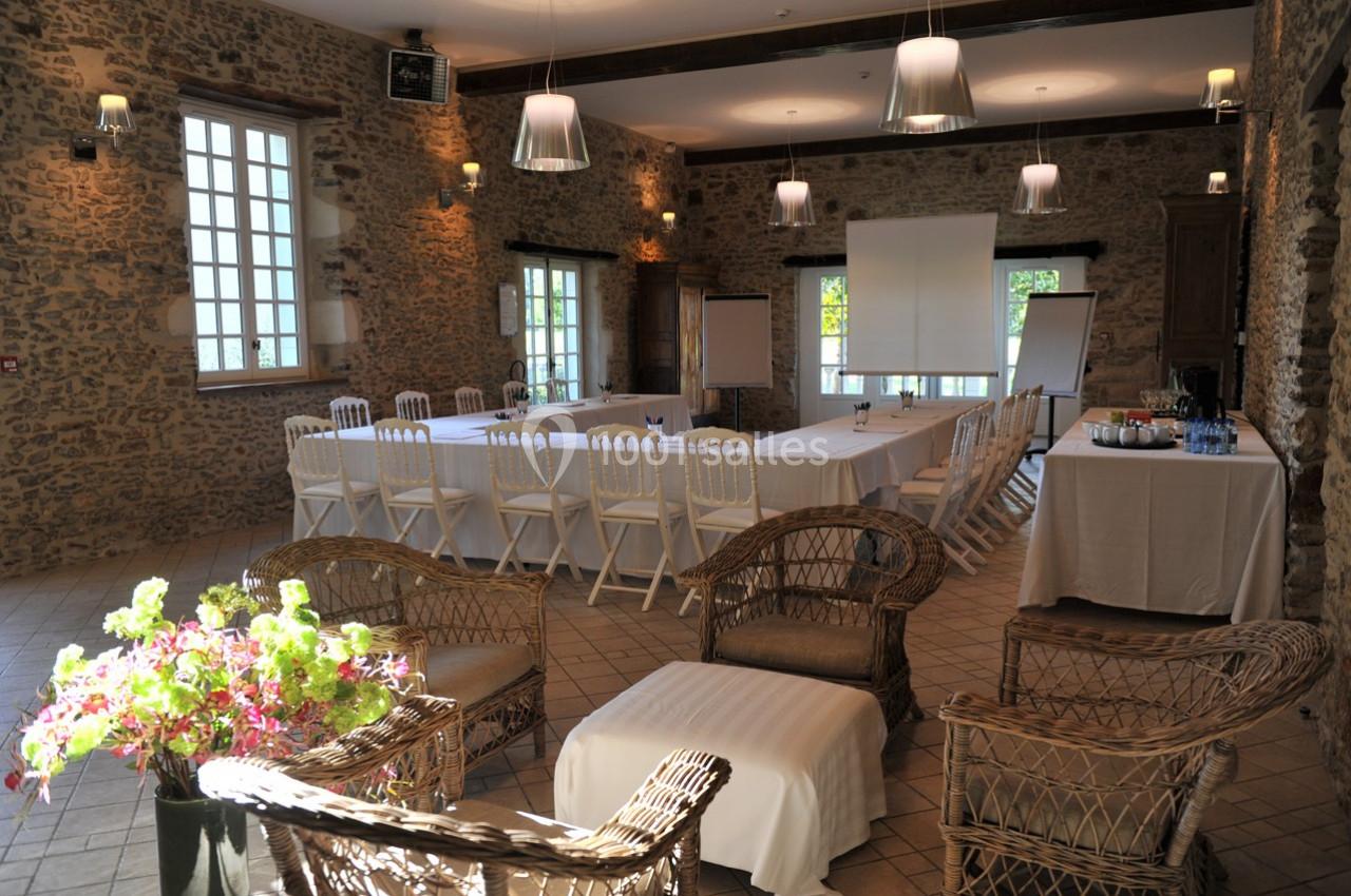 Salle de réunion lumineuse avec murs en pierre, tables disposées en U, chaises blanches et matériel de présentation.