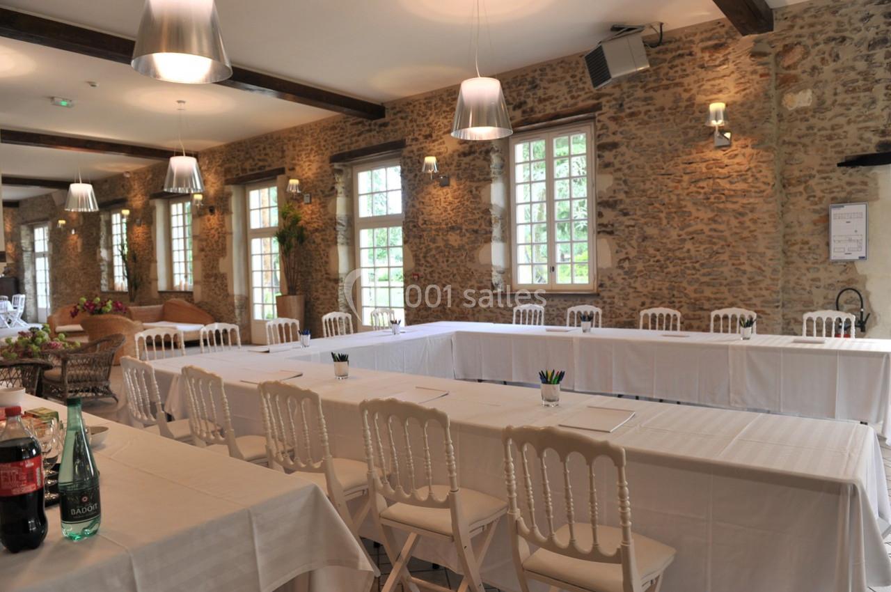 Salle de réunion lumineuse avec murs en pierre, tables disposées en U et chaises blanches.