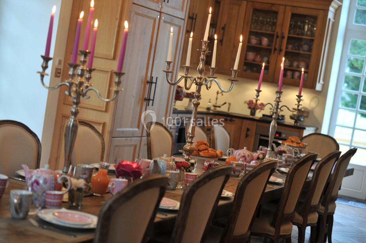 Table dressée avec vaisselle colorée, chandeliers allumés et viennoiseries, dans une cuisine en bois lumineuse.