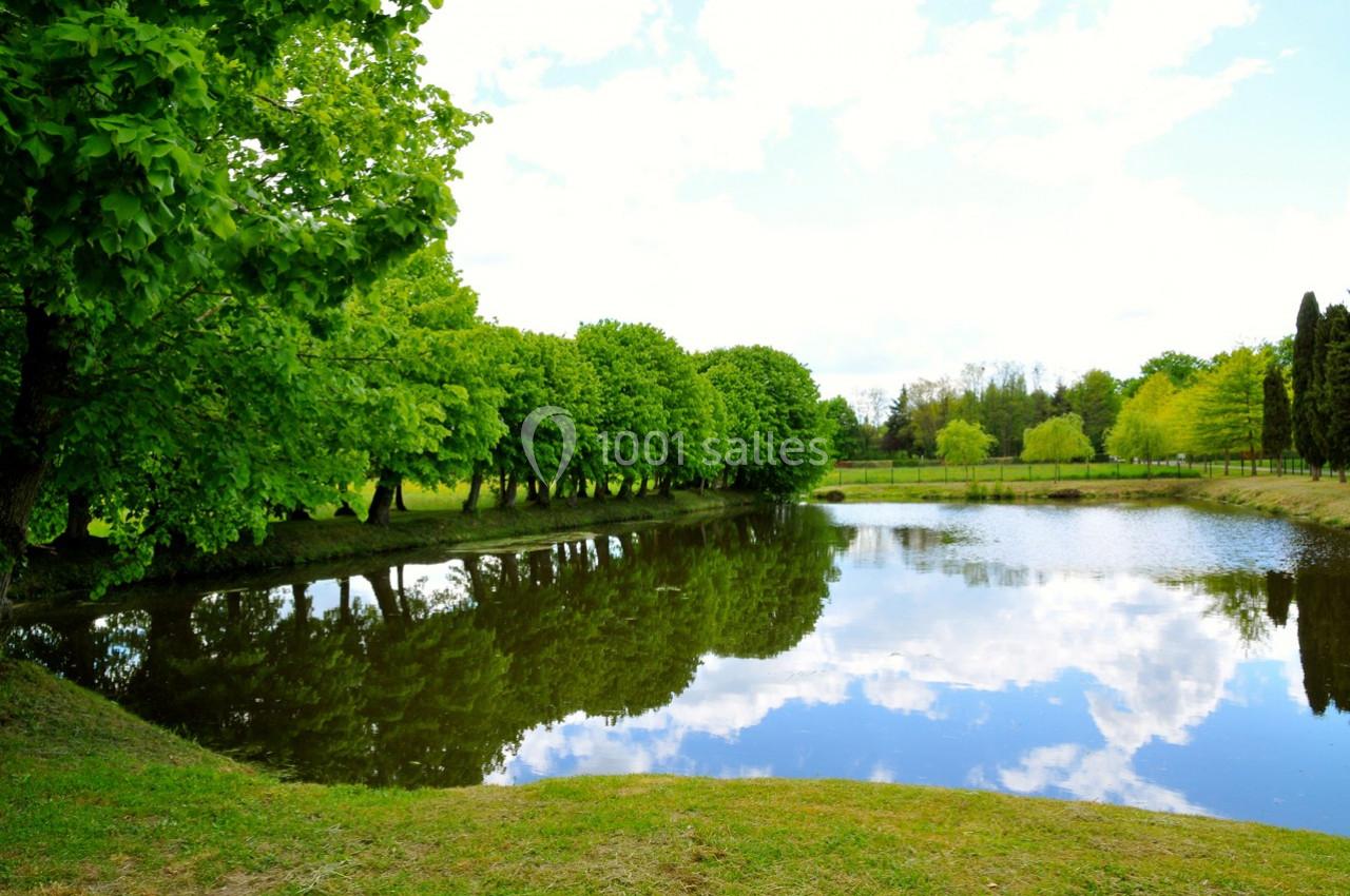 Étang entouré d'arbres avec leur reflet visible dans l'eau sous un ciel partiellement nuageux.