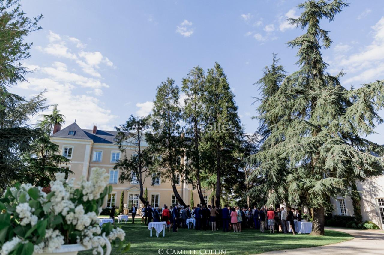 Groupe de personnes rassemblées dans le jardin d'un grand bâtiment entouré d'arbres par une journée ensoleillée.