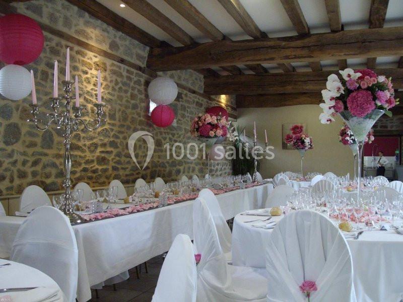 Salle de réception décorée avec des tables dressées, des chandeliers et des arrangements floraux roses et blancs.
